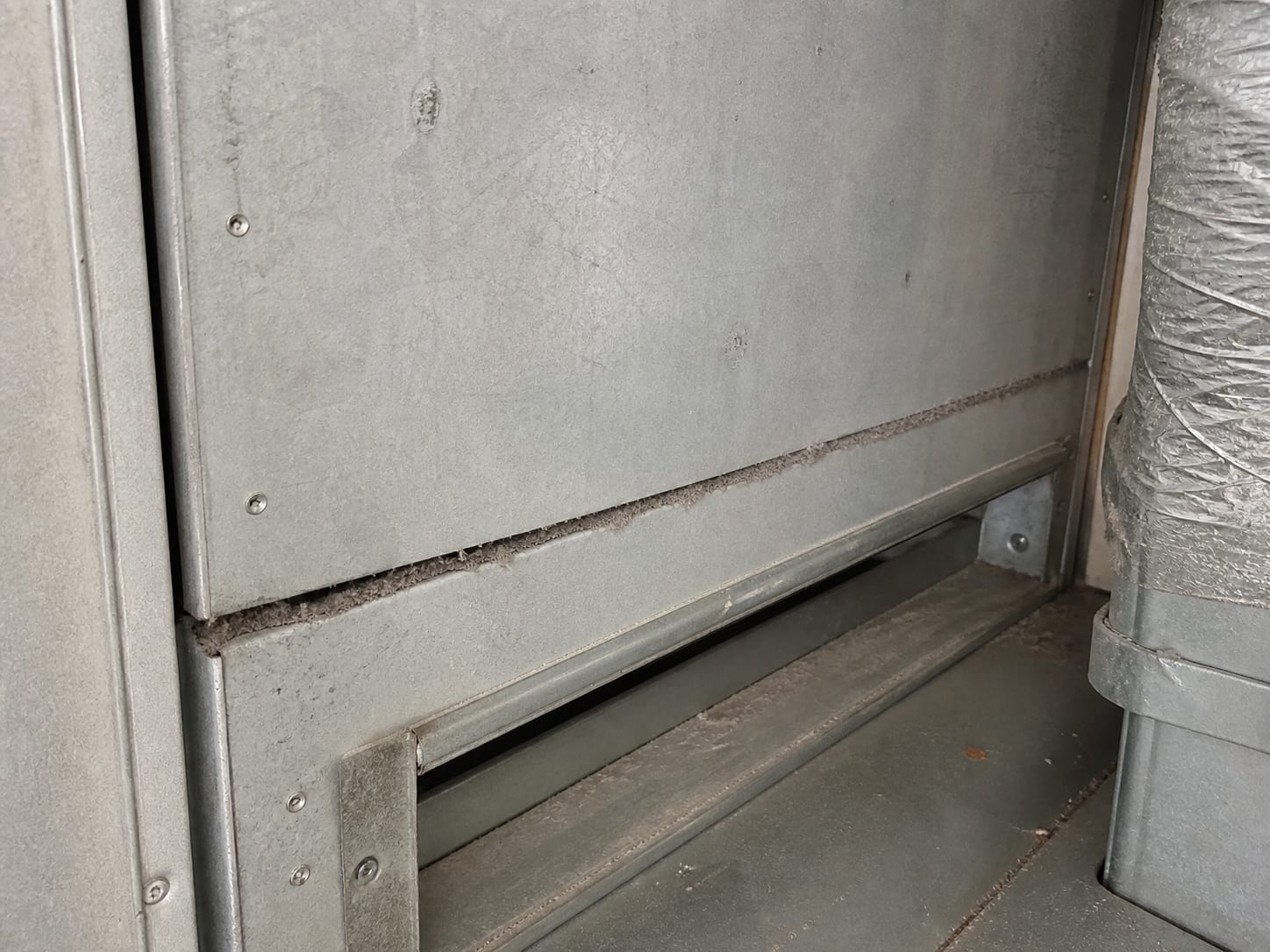 A close view inside the mechanical closet of an East Windsor townhome where an unsealed sheet metal seam at the return plenum carries a dust line drawn along the joint and the filter slot sits empty
