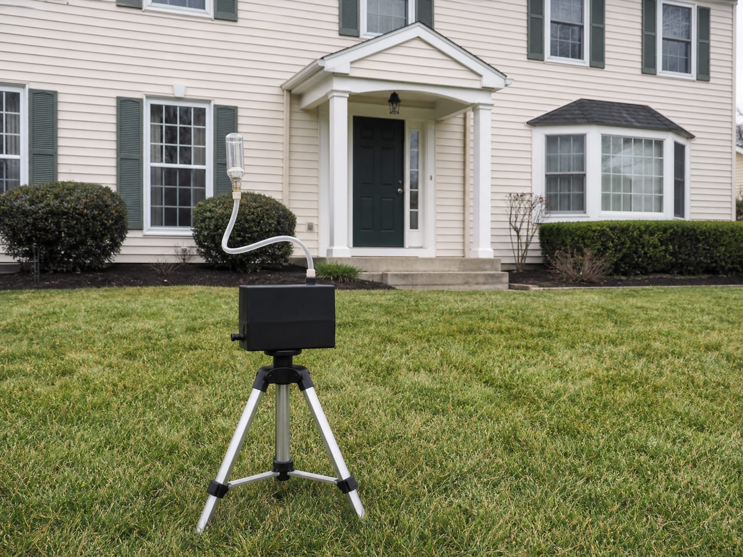 An outdoor air sampling pump standing on a tripod on the lawn outside a West Windsor, New Jersey home with the front entry visible behind it