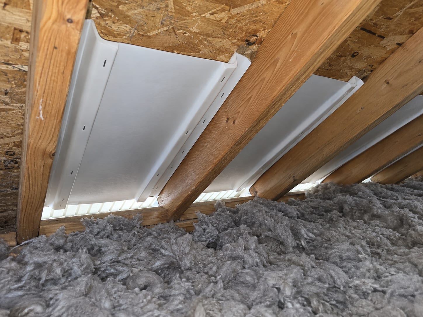 The eave edge of a Bridgewater, New Jersey attic where the soffit intake opening has ventilation baffle channels and insulation held back from it