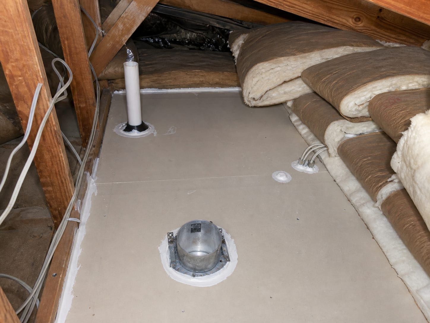 A wider view along the attic floor of an East Windsor townhome where insulation has been pulled back from a run of joist bays to expose the top of the ceiling drywall, and the fixture housing, pipe penetration, wiring holes and top plate gap have been sealed