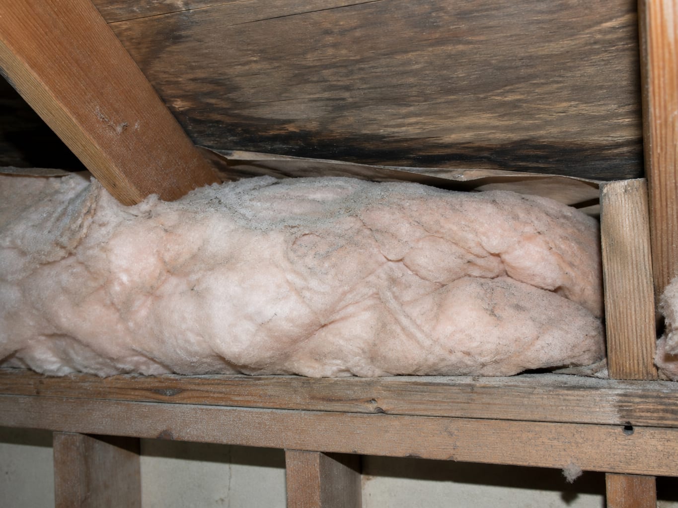 A low eave detail in a Livingston attic where batt insulation has been pushed out over the soffit vent opening and the baffle behind it is crushed flat, closing the intake