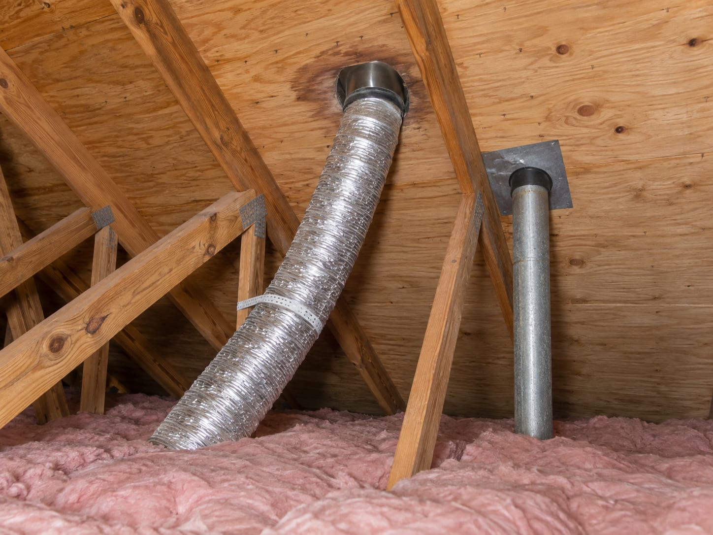 Attic in a Robbinsville, New Jersey house with a flexible bath fan duct running up the underside of the roof sheathing to a roof vent, and darker staining on the boards around it