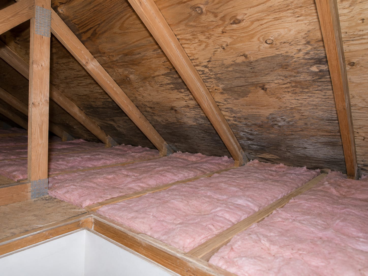 Unfinished attic in a Robbinsville, New Jersey house with untouched fiberglass insulation on the floor and dark stains on the plywood roof sheathing above