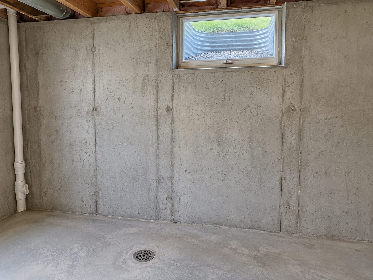 A Bridgewater, New Jersey basement wall with a small window and window well above a floor drain, showing how low the lowest floor sits against outside grade