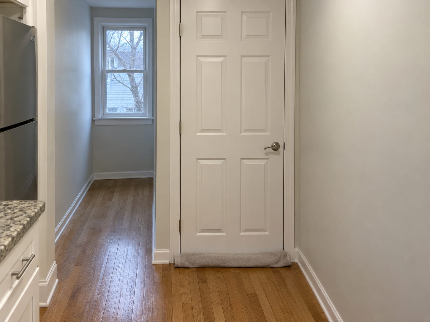 A closed paneled interior door at the top of a New Jersey home's basement stairs, in a clean hallway with a rolled towel along the bottom gap