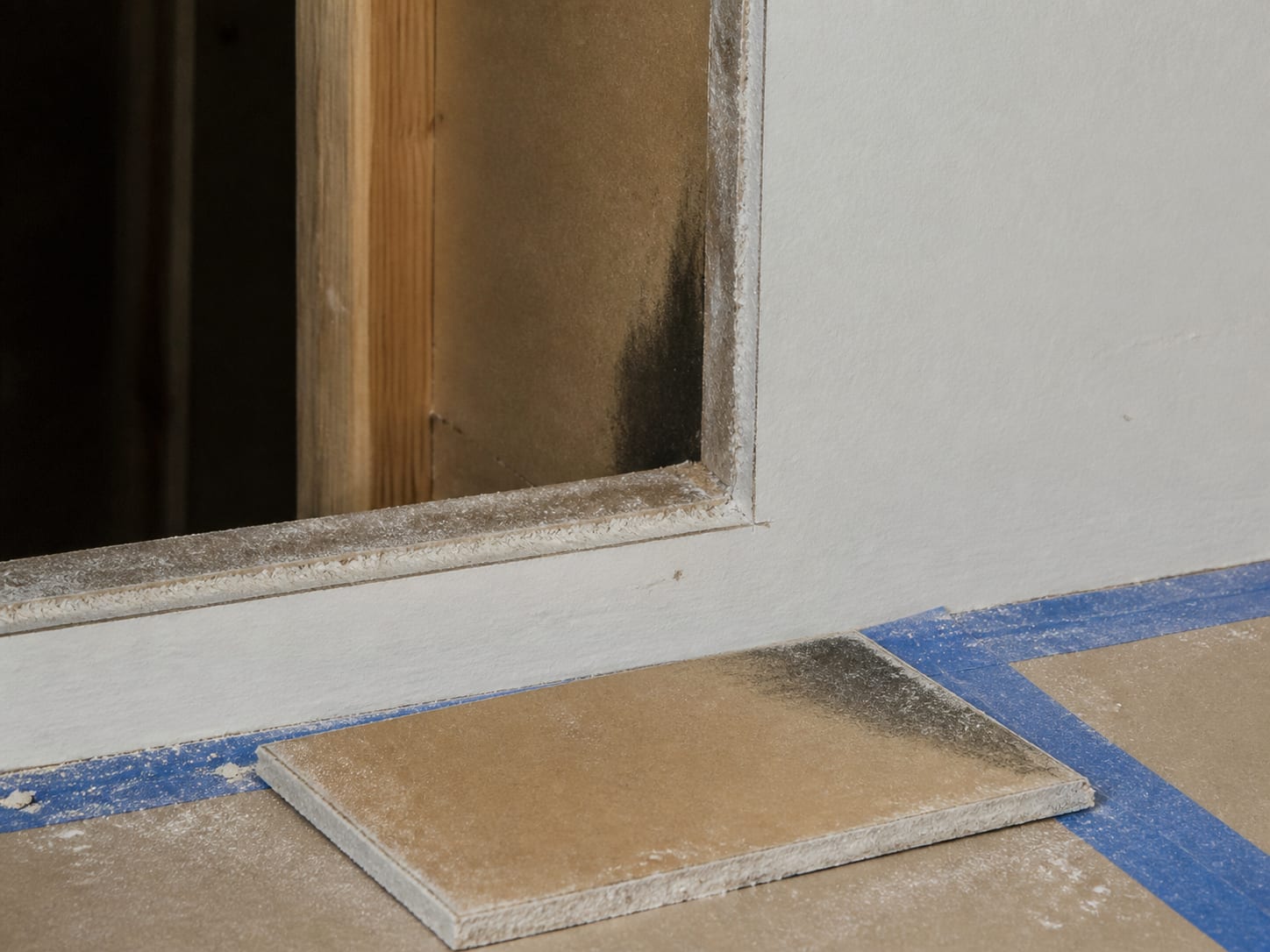 A close view of the square cut edge left in a Livingston bathroom wall, showing discoloration on the back paper face of the drywall fading to clean gypsum where the moisture stopped