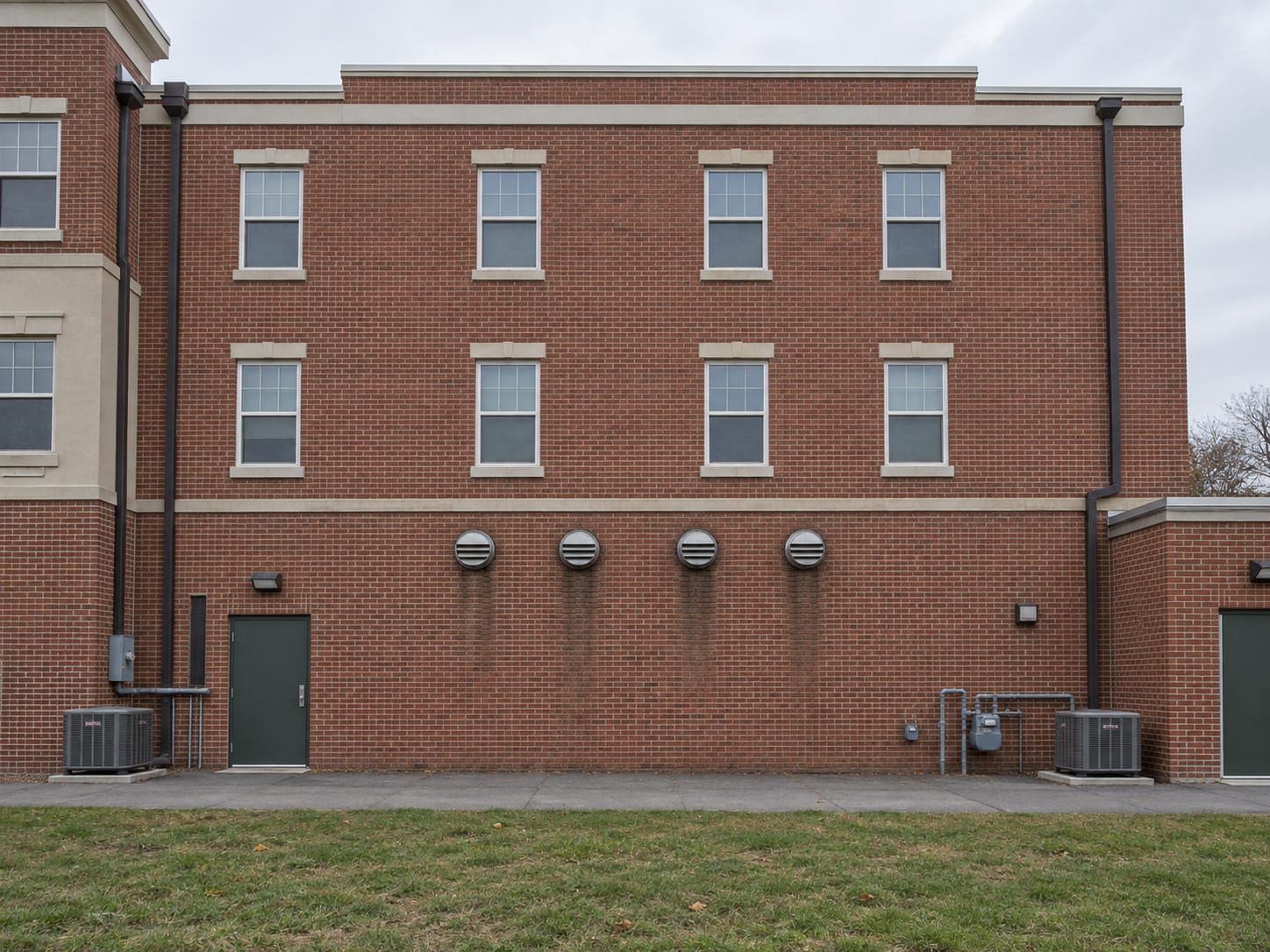 Rear wall of a mixed-use building in Robbinsville, New Jersey with several louvered dryer exhaust caps in the brick and a flat roof edge above