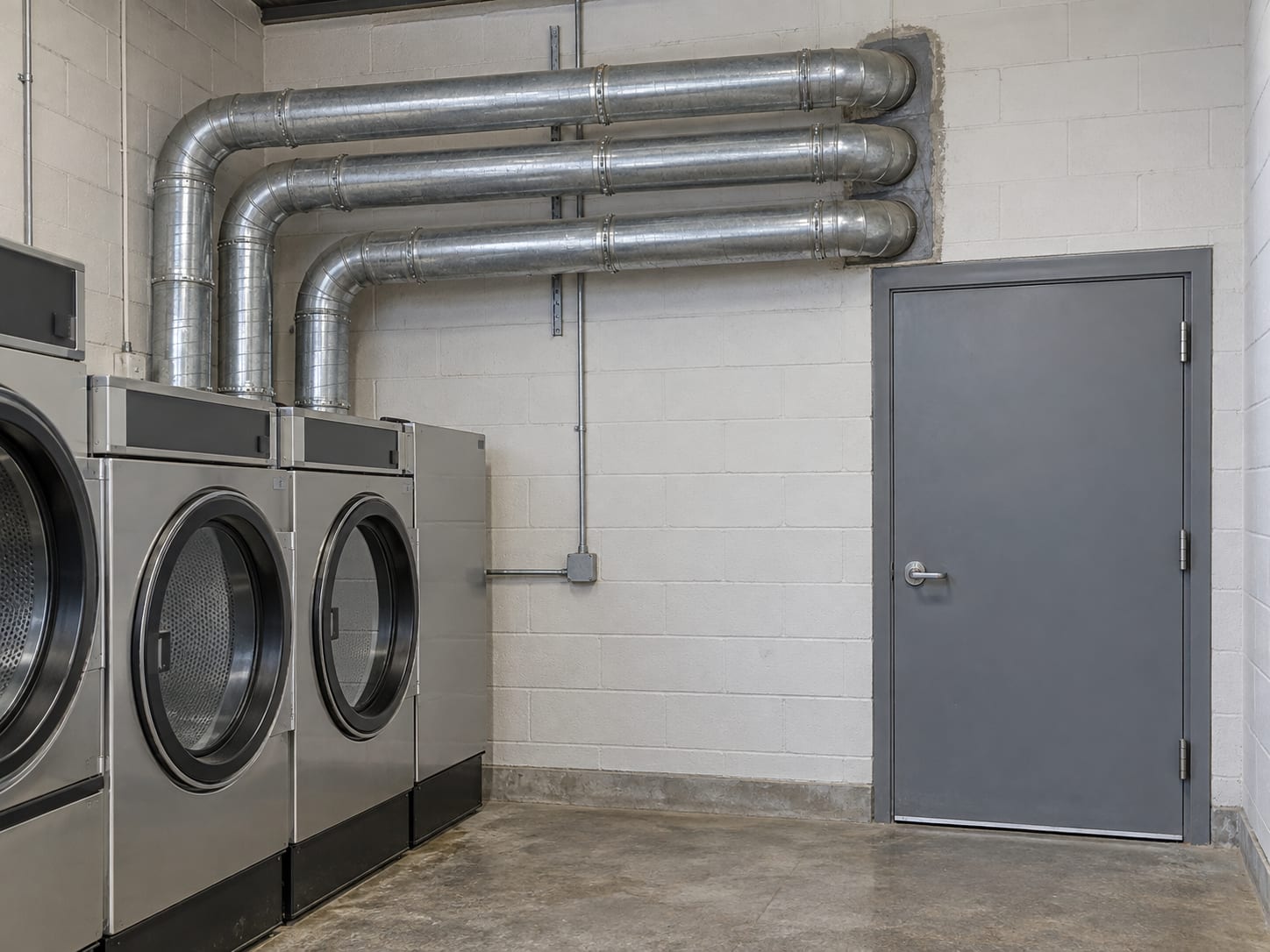 Wall of a separate laundry room in a Robbinsville, New Jersey building with a closed solid steel door and rigid metal ducts passing through the masonry to the outside