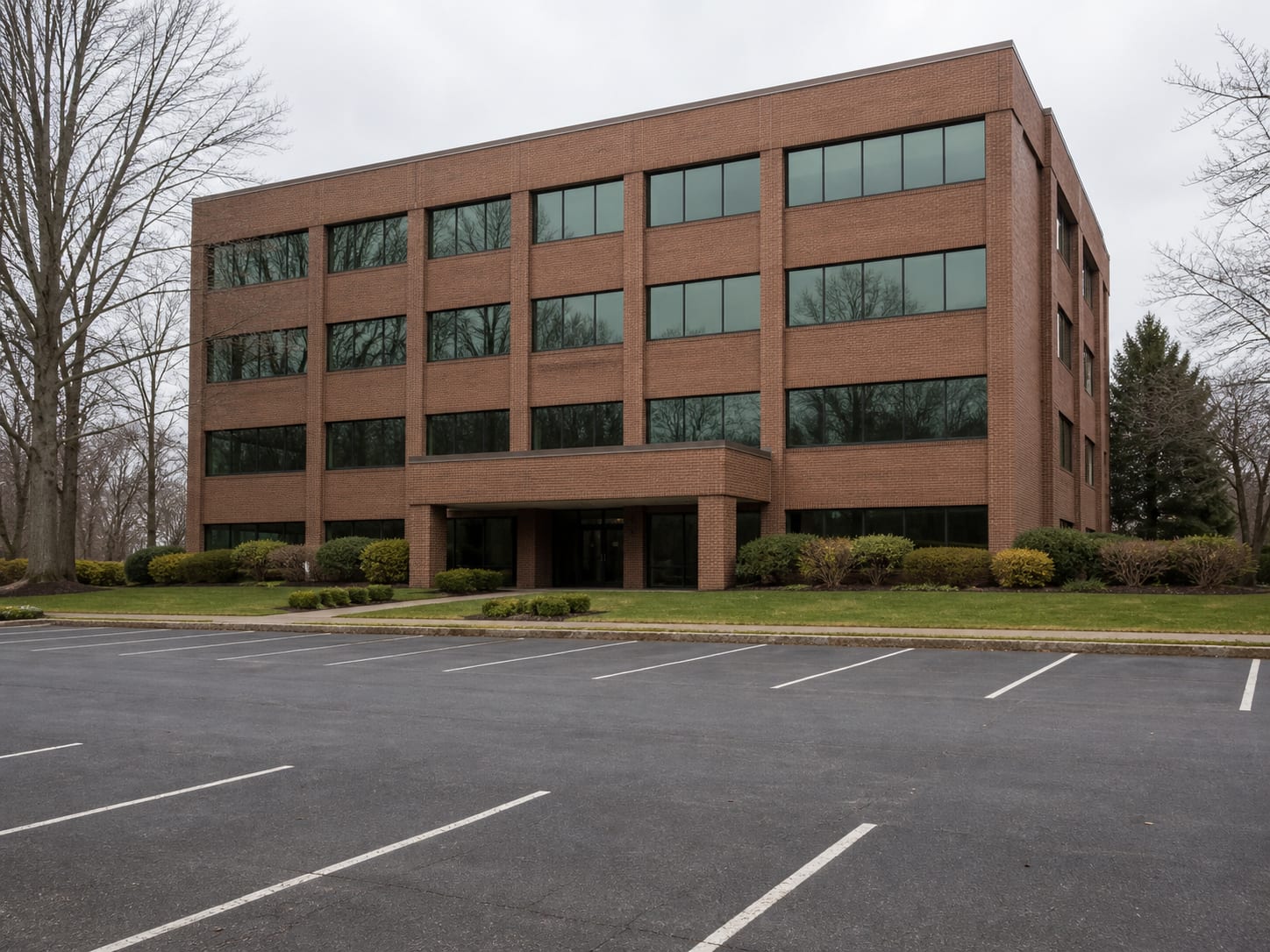A four storey red brown brick and tinted glass office building set among mature trees with a surface parking area, in Warren, New Jersey