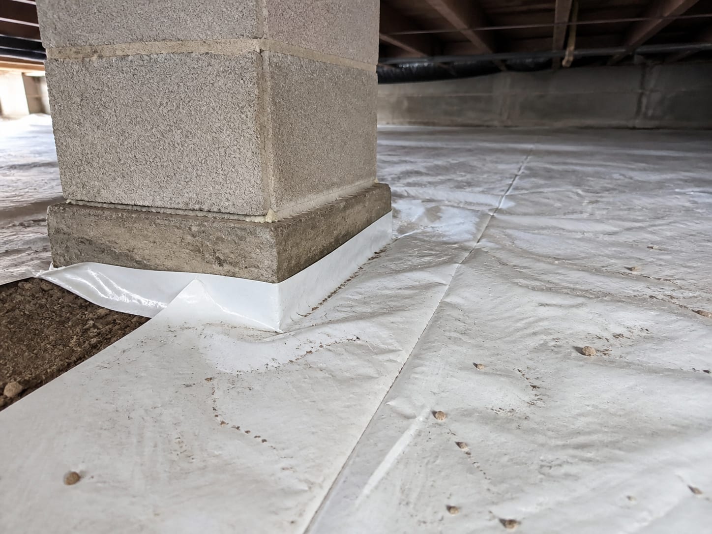 White vapor barrier sheeting cut and overlapped neatly around a masonry block pier footing on a crawl space floor, in Warren, New Jersey