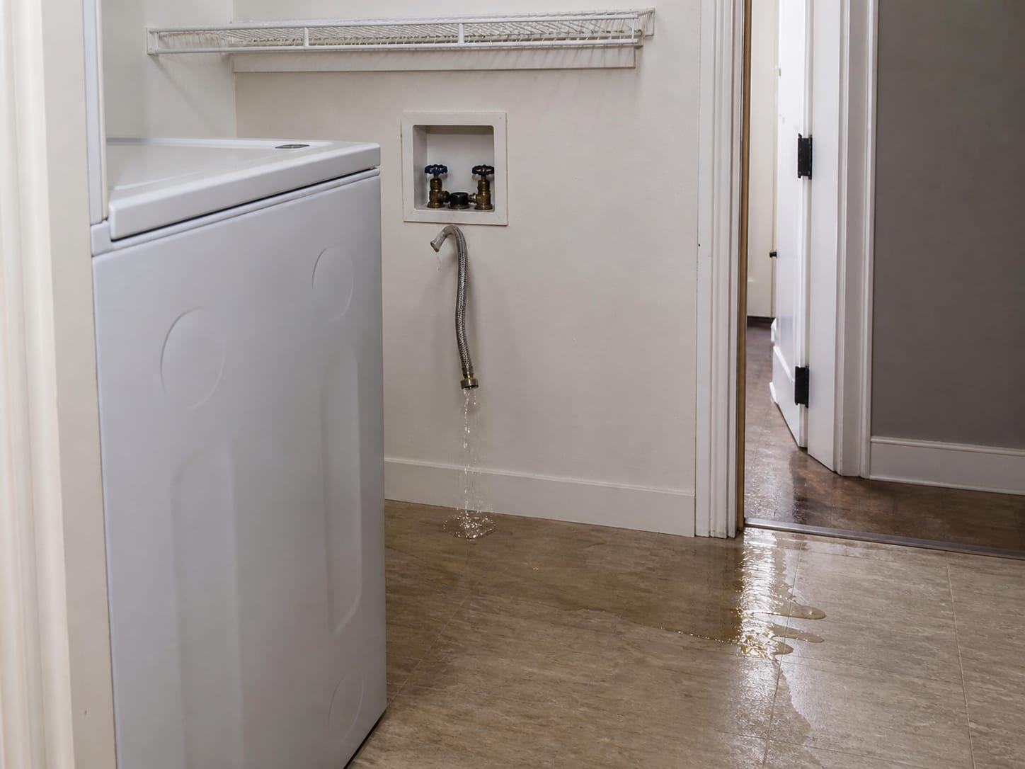 A washing machine pulled forward in a Livingston laundry alcove with both supply stop valves closed, a failed braided hose hanging loose, and water tracked across the floor