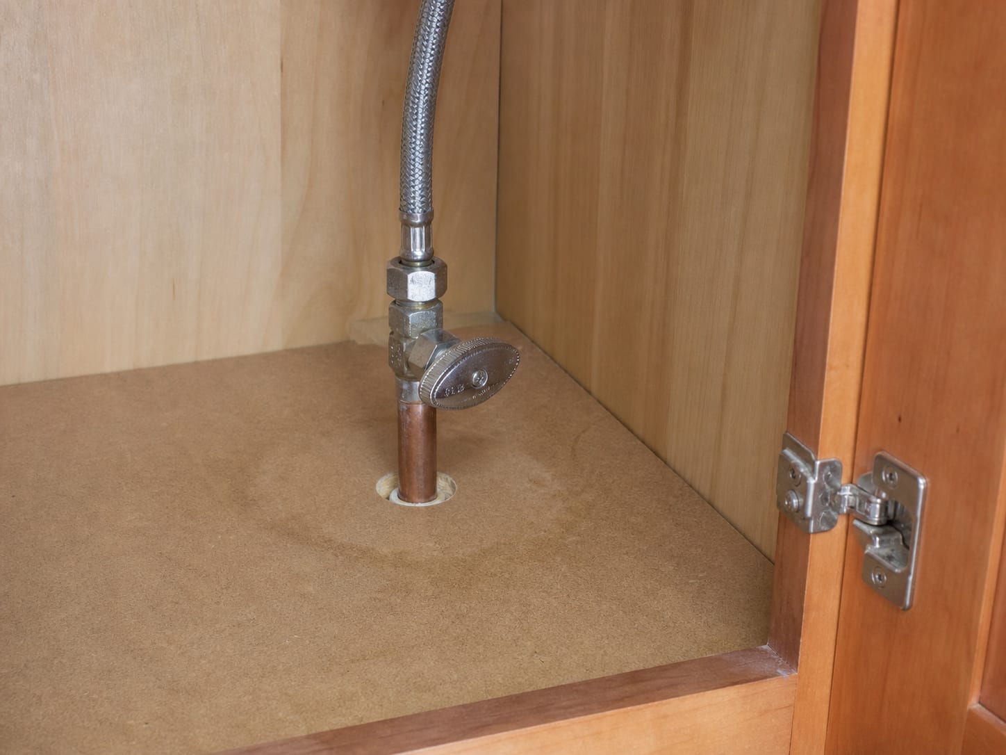 A small chrome fixture shutoff valve on a copper supply line beneath a bathroom vanity, cabinet door open, everything dry, in Plainsboro, New Jersey