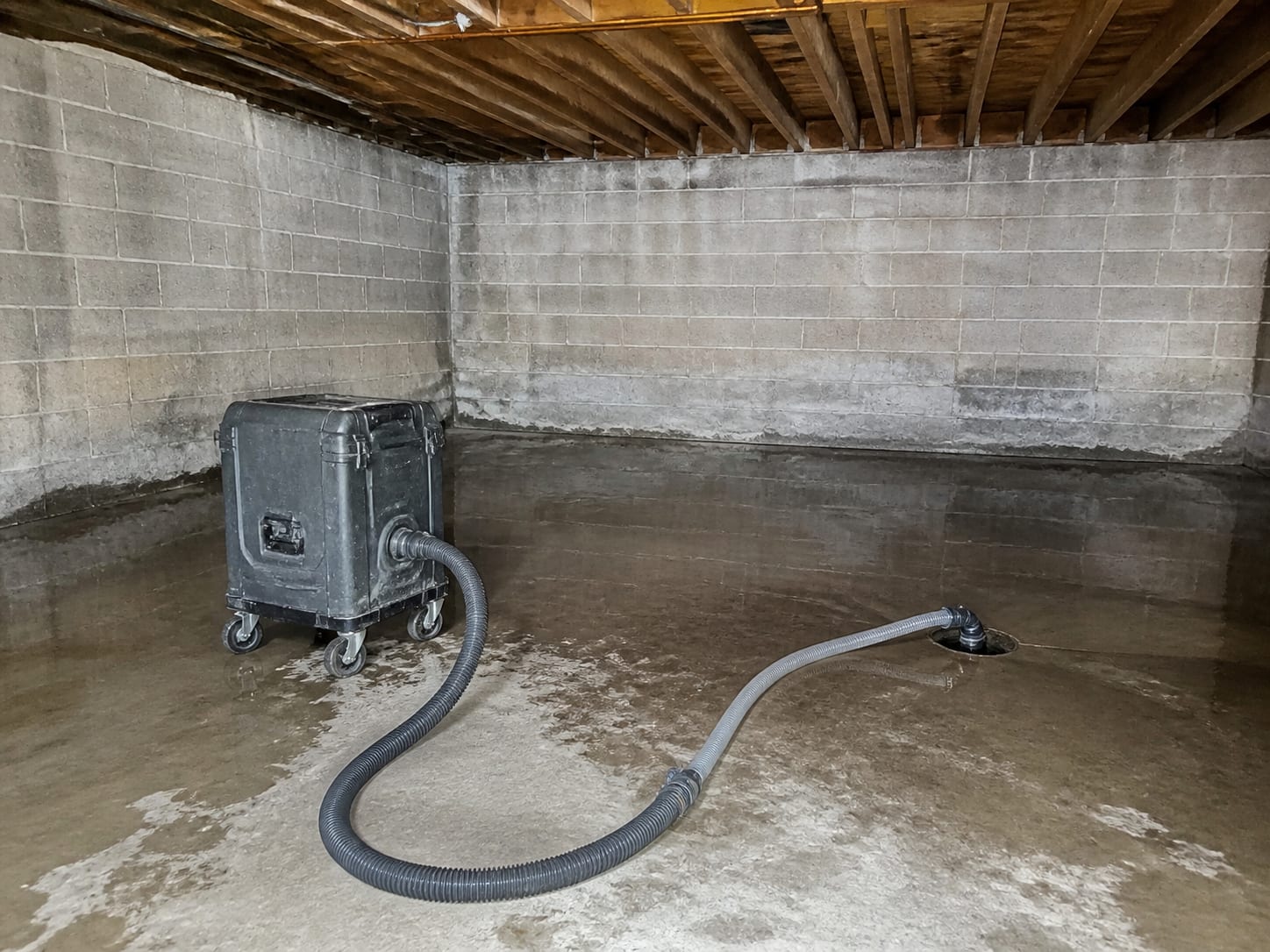 A portable extraction unit standing on a wet concrete floor with vacuum and discharge hoses run out toward a floor drain, in Warren, New Jersey
