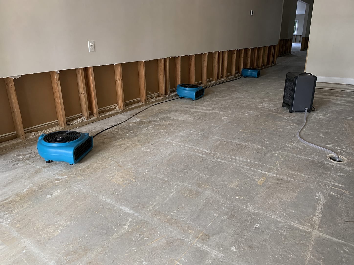 Air movers and a dehumidifier positioned along a stripped lower level wall in a West Windsor, New Jersey home with the drywall cut to a clean horizontal line above the slab