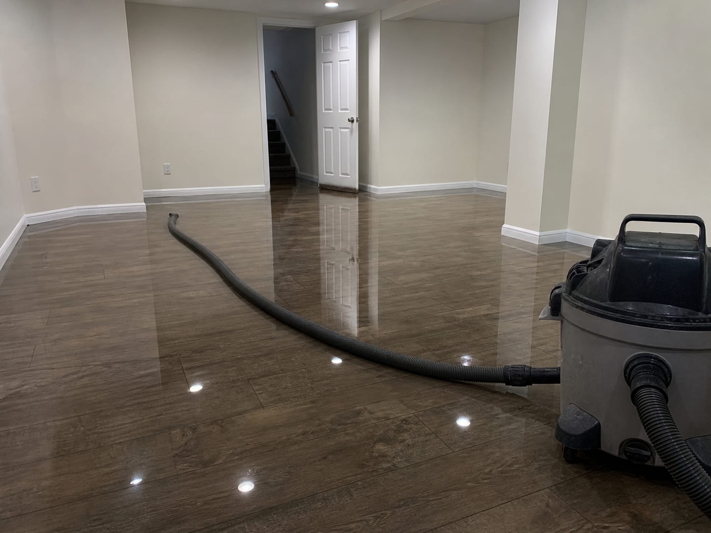 Standing water across a lower level room in a West Windsor, New Jersey home with an extraction hose lying on the floor and running back to a portable extractor