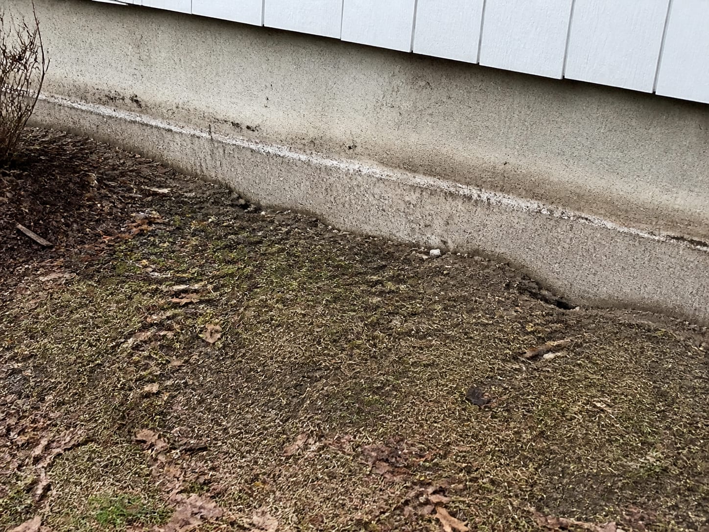 A silt line and flattened grass marking how high water stood against the exposed foundation course of a house on a sloping lot, in Warren, New Jersey