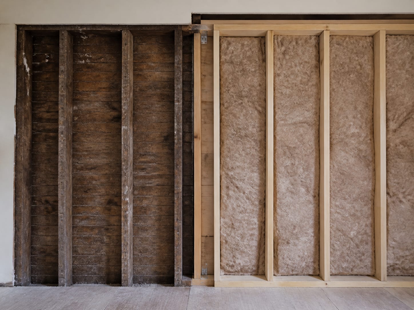 An opened wall showing shallow older framing and obsolete construction on one side of a stud line and deeper modern framing on the other, the difference plain at the junction, in Alpine, New Jersey