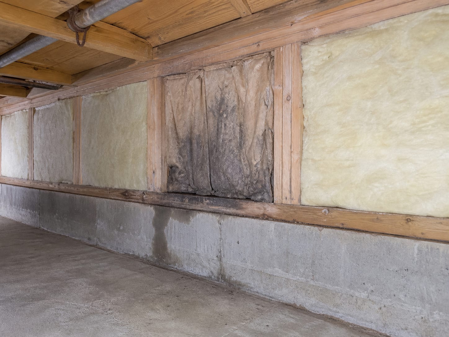 The junction of floor framing and a foundation wall in a utility space, with a single joist bay noticeably darker and stained while the bays either side are clean and pale, in Alpine, New Jersey