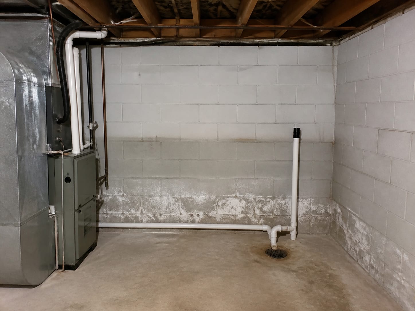A utility corner of a Livingston basement with a painted block foundation wall, a staining line and efflorescence, a floor drain and a condensate line, everything intact