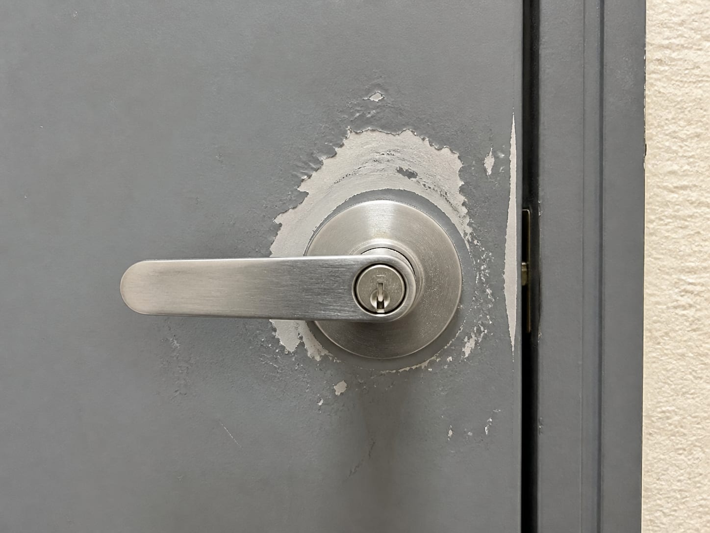 A tight straight on view of the closed lever handle and lock face of a painted steel mechanical room door in an apartment building common corridor, the door shut, in Plainsboro, New Jersey
