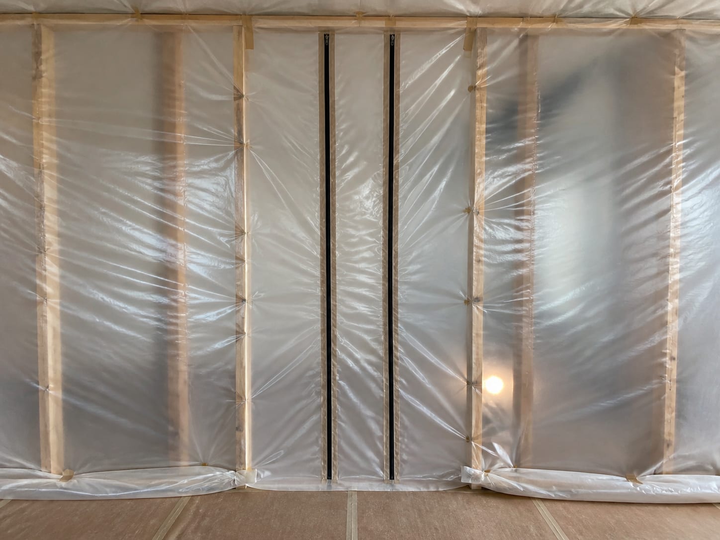 A close view of a zippered containment panel with the poly sheeting pulled tight and dimpled inward around the seam under negative pressure, in Warren, New Jersey