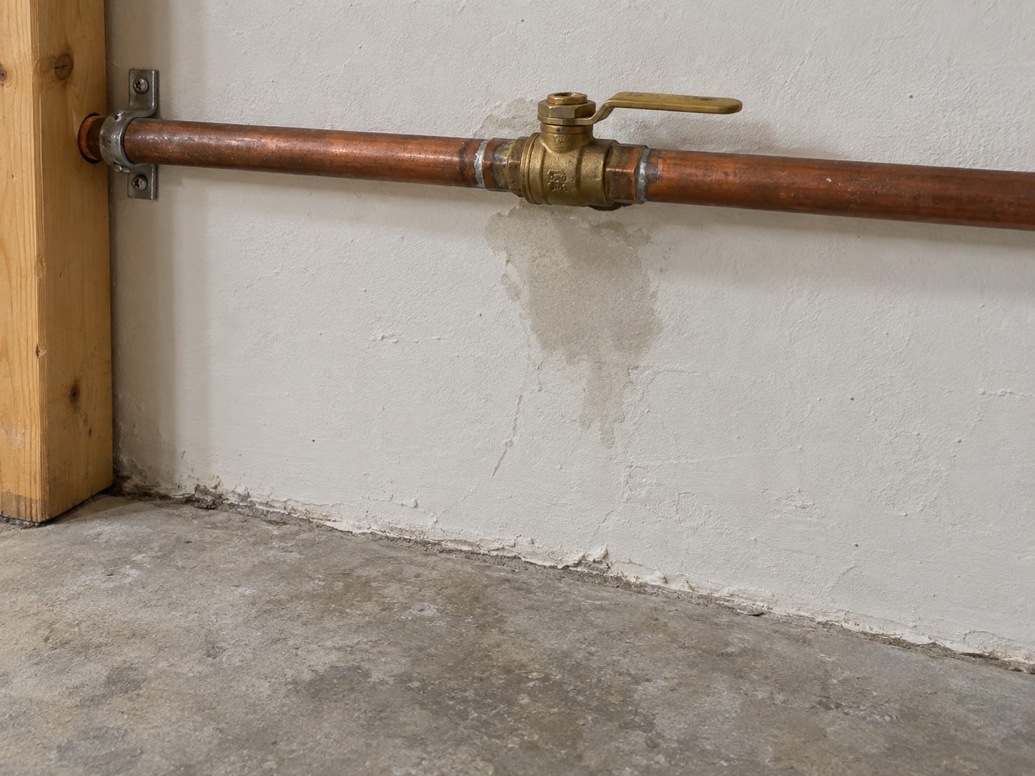 Utility corner of a Robbinsville, New Jersey basement with a copper supply pipe, a closed quarter-turn shutoff valve and a small damp stain on the drywall below