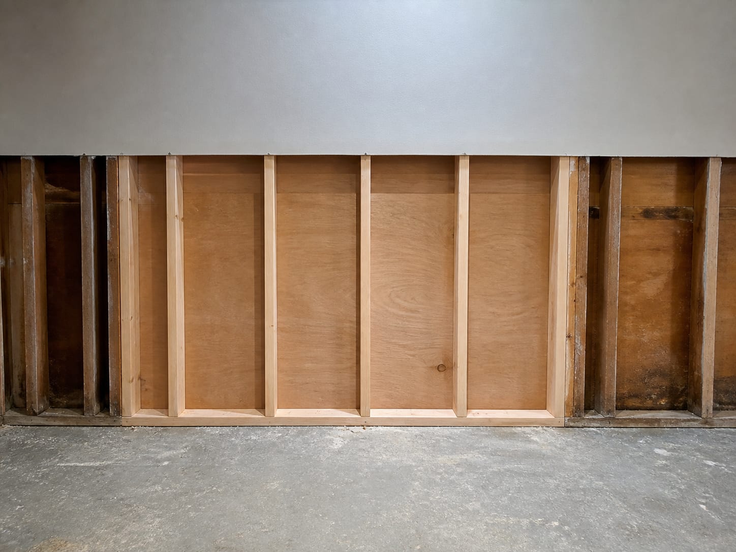An opened wall bay after cleaning, the framing pale and uniform with the surrounding untouched framing darker, and the cavity empty and dry, in Alpine, New Jersey