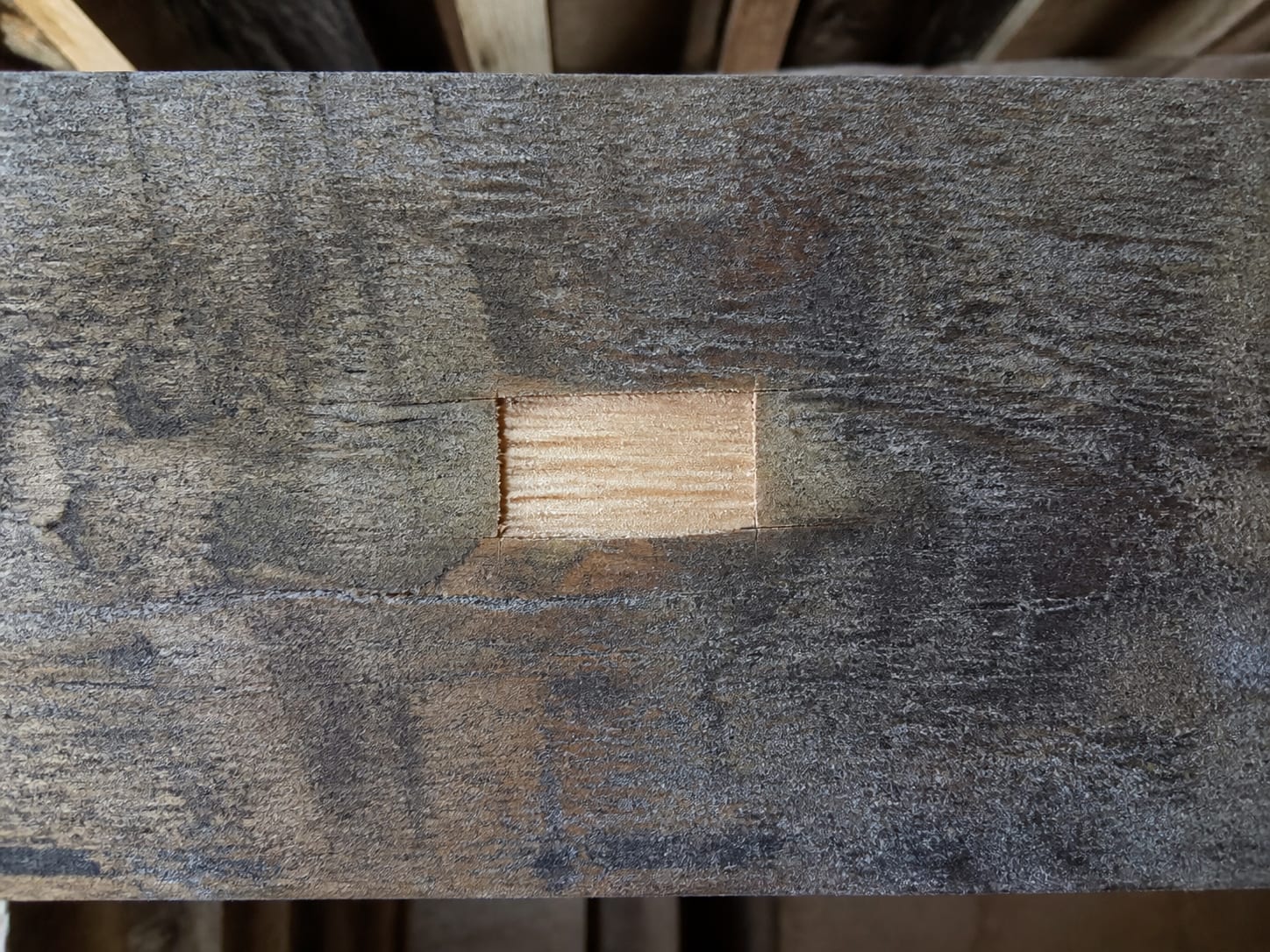 A stained timber joist with one small clean rectangle where a surface sample has been lifted, the surrounding wood still dark and mottled, in Alpine, New Jersey