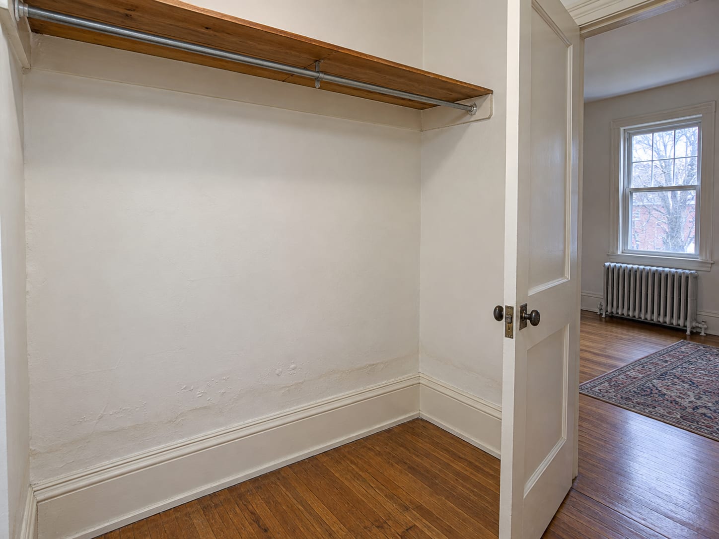 Empty closet in an older Trenton, New Jersey house with clean painted plaster and paint blistering low above the baseboard