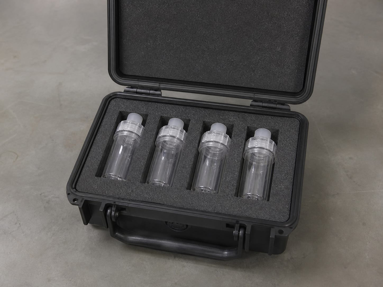 Several clear sealed unlabelled spore trap cassettes seated upright in the moulded foam of an open transport case on a plain surface, in Warren, New Jersey