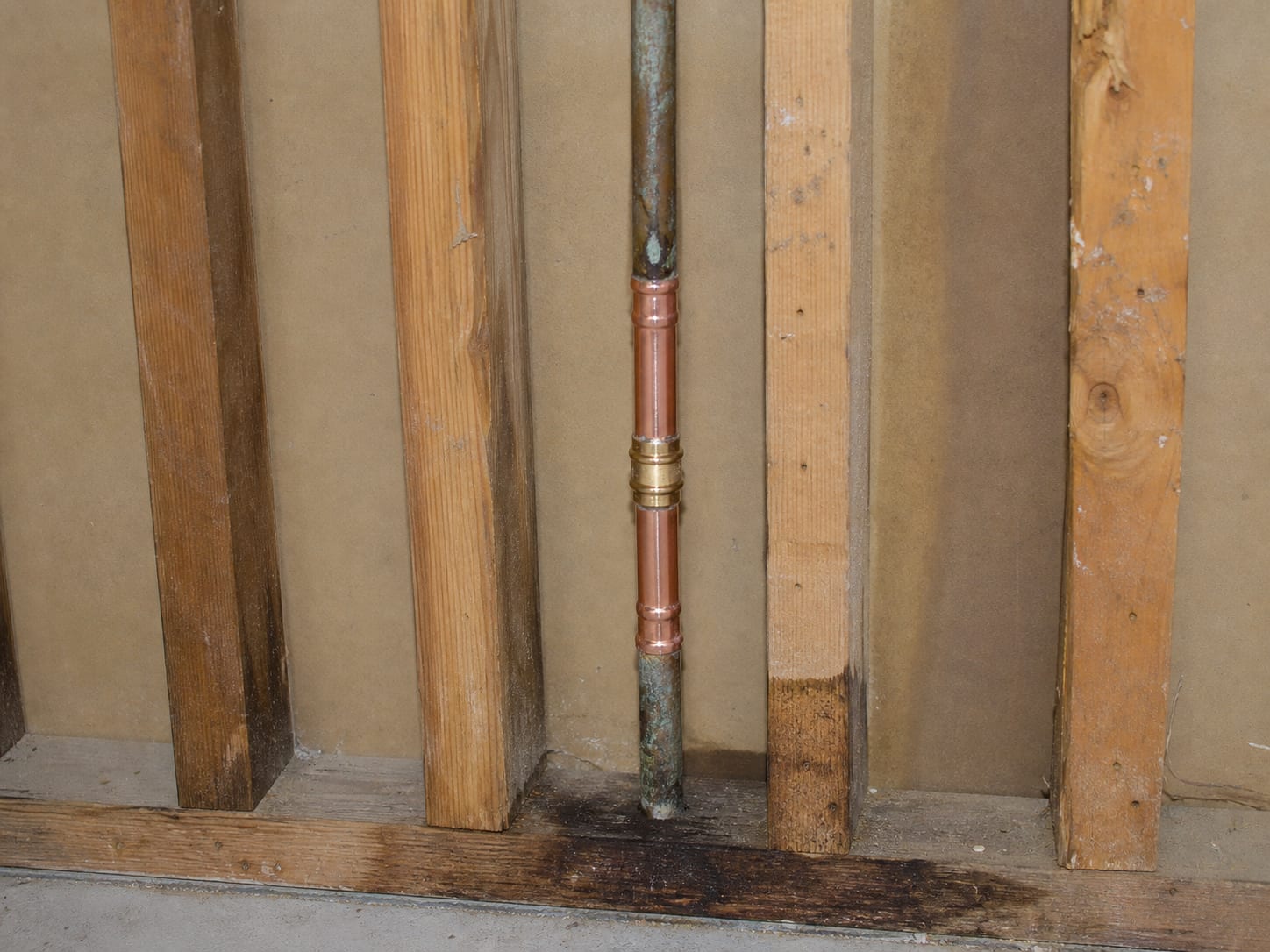 A close view inside an open stud bay in an East Windsor townhome where a bright new section of supply pipe and a fresh fitting have been spliced into the older line above a stained bottom plate