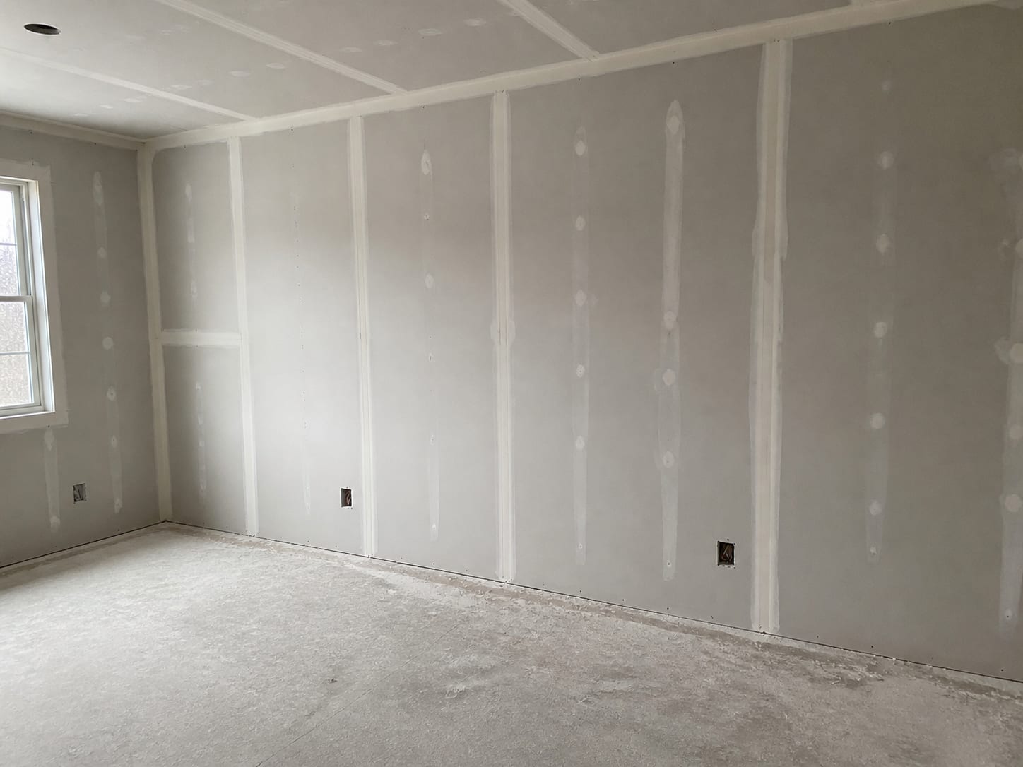 A rebuilt room with new plasterboard hung and the joints taped and set but unpainted, outlet boxes left open in the wall and the rough work still visible, in Plainsboro, New Jersey