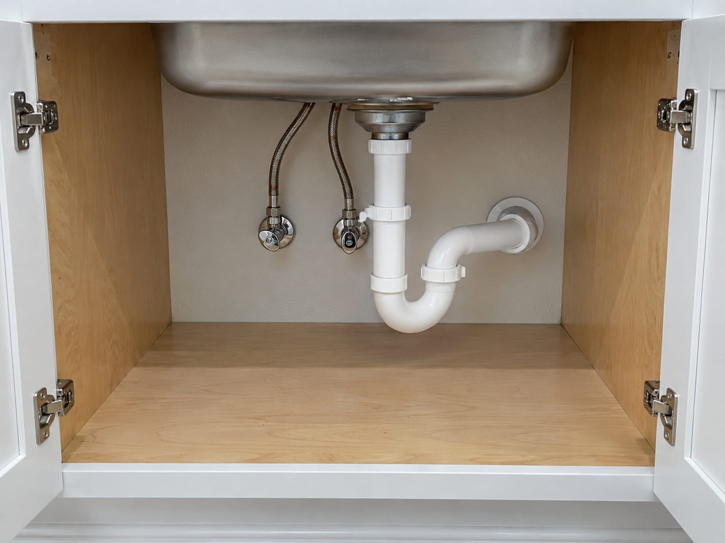 An open sink base cabinet in a New Jersey kitchen with new supply lines and a new drain trap, and a clean dry cabinet floor