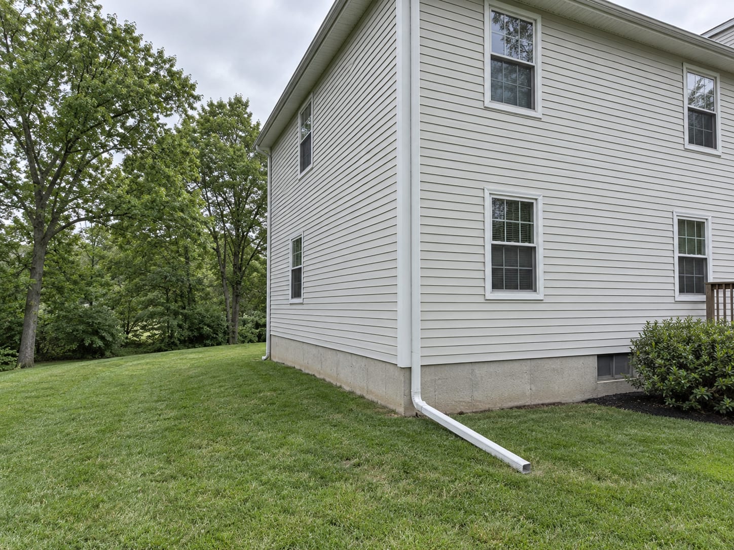 A gutter downspout with an extension discharging onto sloped lawn away from the foundation of a New Jersey colonial house