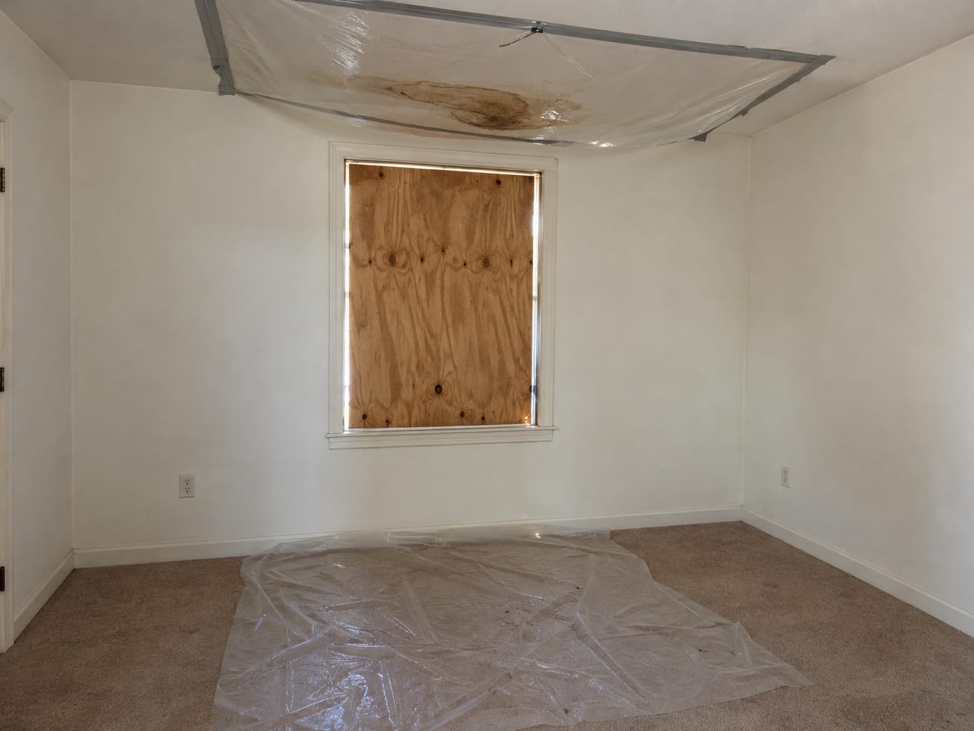 Upstairs bedroom in a Robbinsville, New Jersey house with plywood screwed over a window opening and plastic sheeting taped below a wet ceiling stain