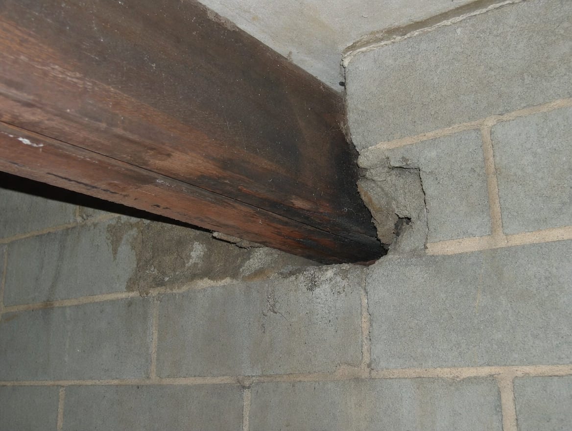 A close view of a darkened floor joist bearing into a concrete-block party wall in a Princeton Junction townhouse, the point where one unit's framing meets the shared structure