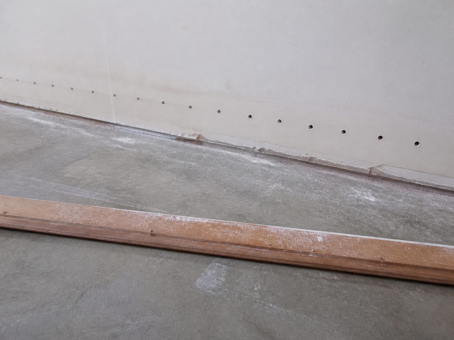 A row of small drilled holes at the base of a wall below the baseboard line with the baseboard removed, in Warren, New Jersey