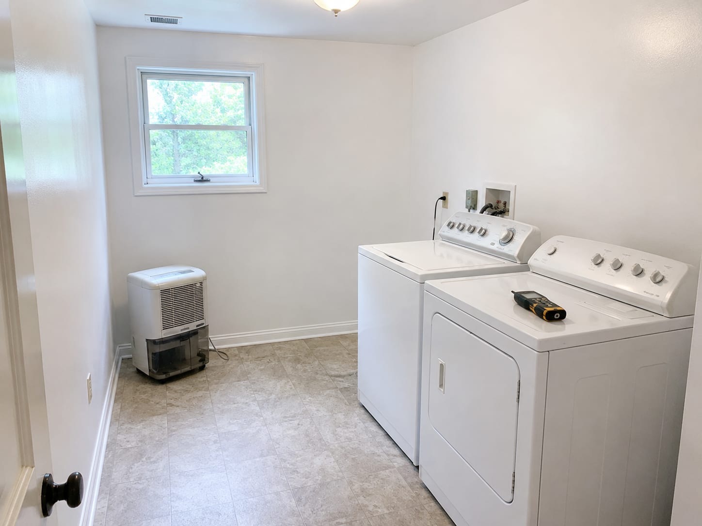 Freshly painted white laundry room in a New Jersey home after mold removal showing clean drywall, new baseboard trim, and a running dehumidifier with a moisture meter resting on the dryer