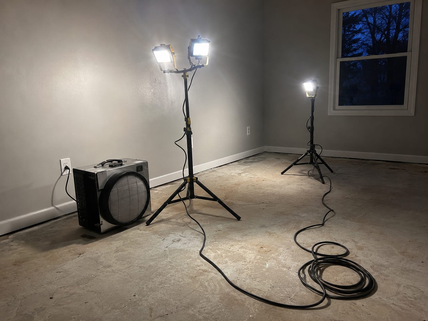 A clean, treated residential room at night lit by portable LED work lights with a HEPA air scrubber staged and ready, conveying around-the-clock emergency response