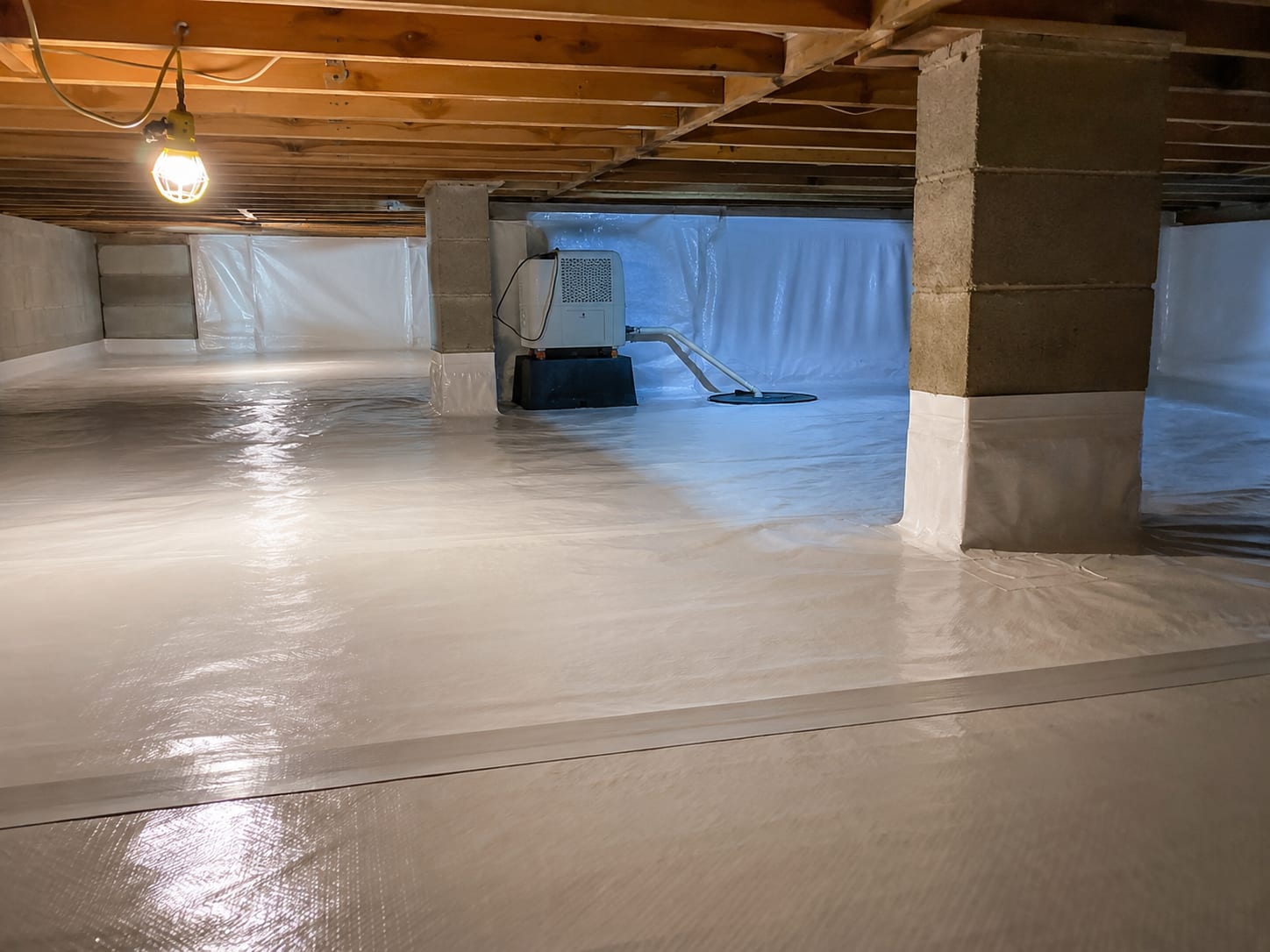 Clean encapsulated crawl space under a New Jersey residential home showing bright white vapor barrier lining walls and floor with a small dehumidifier and clean support piers visible