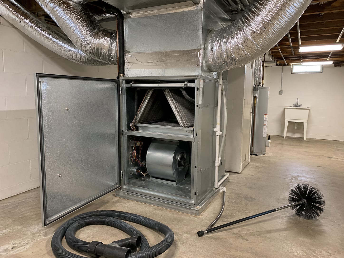 Wide view of an open residential HVAC air handler cabinet with clean silver flex ducts and a freshly vacuumed interior compartment in a finished New Jersey basement utility room