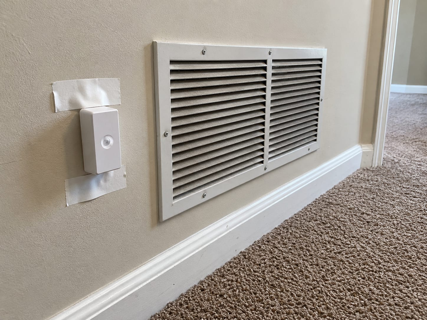 Air sampling cassette taped near a wall-mounted HVAC return vent in a New Jersey home hallway