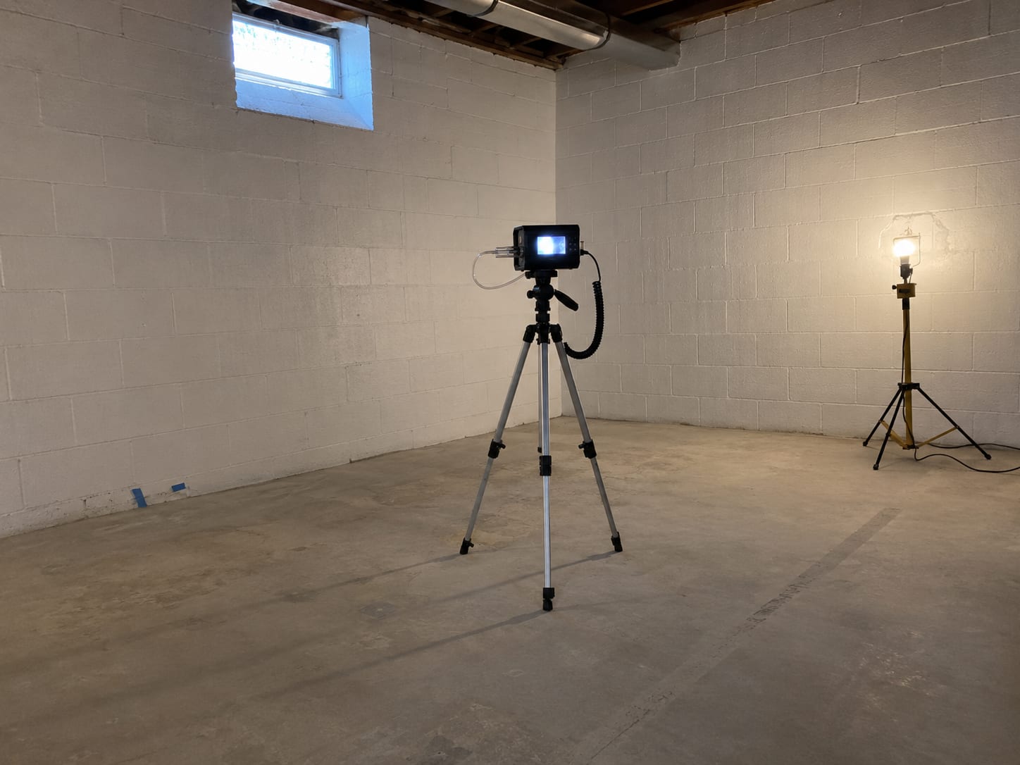 Air sampling pump on tripod positioned inside a remediated room with bare concrete block walls and fresh paint where containment sheeting has been removed after mold remediation