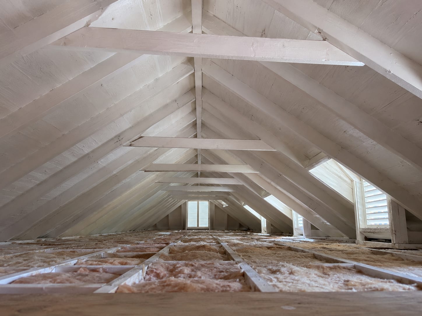Wide view of a remediated residential attic showing clean treated roof sheathing and rafters with white encapsulant coating under natural light from gable vents