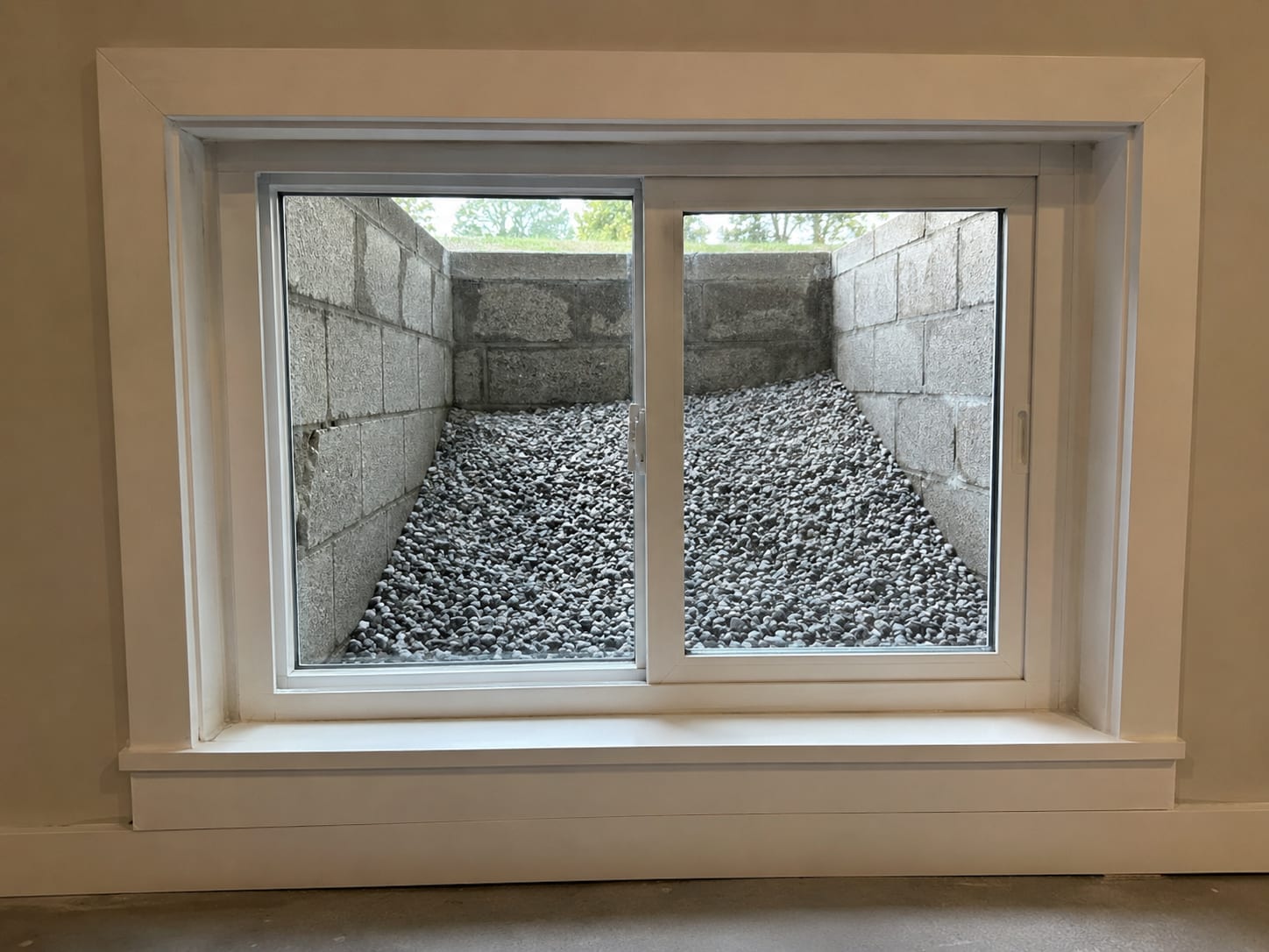 Newly installed egress window with vinyl frame set into a cut concrete block foundation wall with a gravel-filled window well visible outside