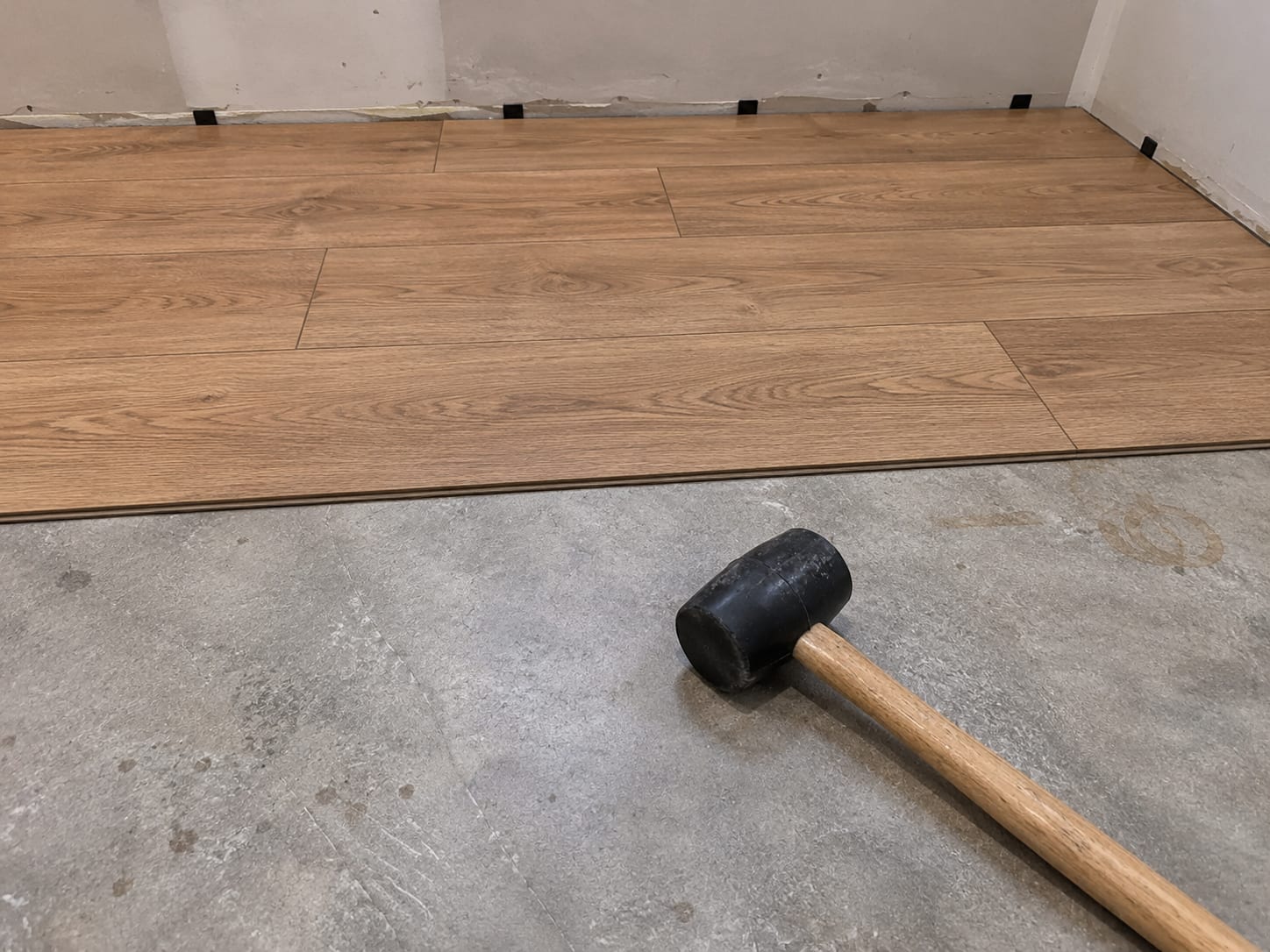 Close-up of luxury vinyl plank flooring being installed on a basement concrete slab with planks snapped together and a rubber mallet nearby