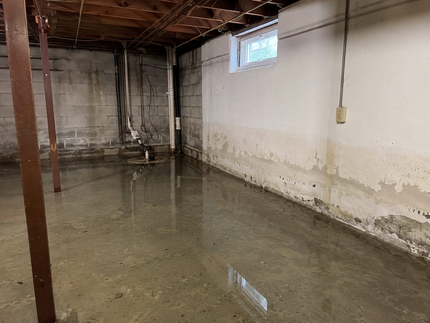 Flooded residential basement interior with standing water on concrete floor near utility area