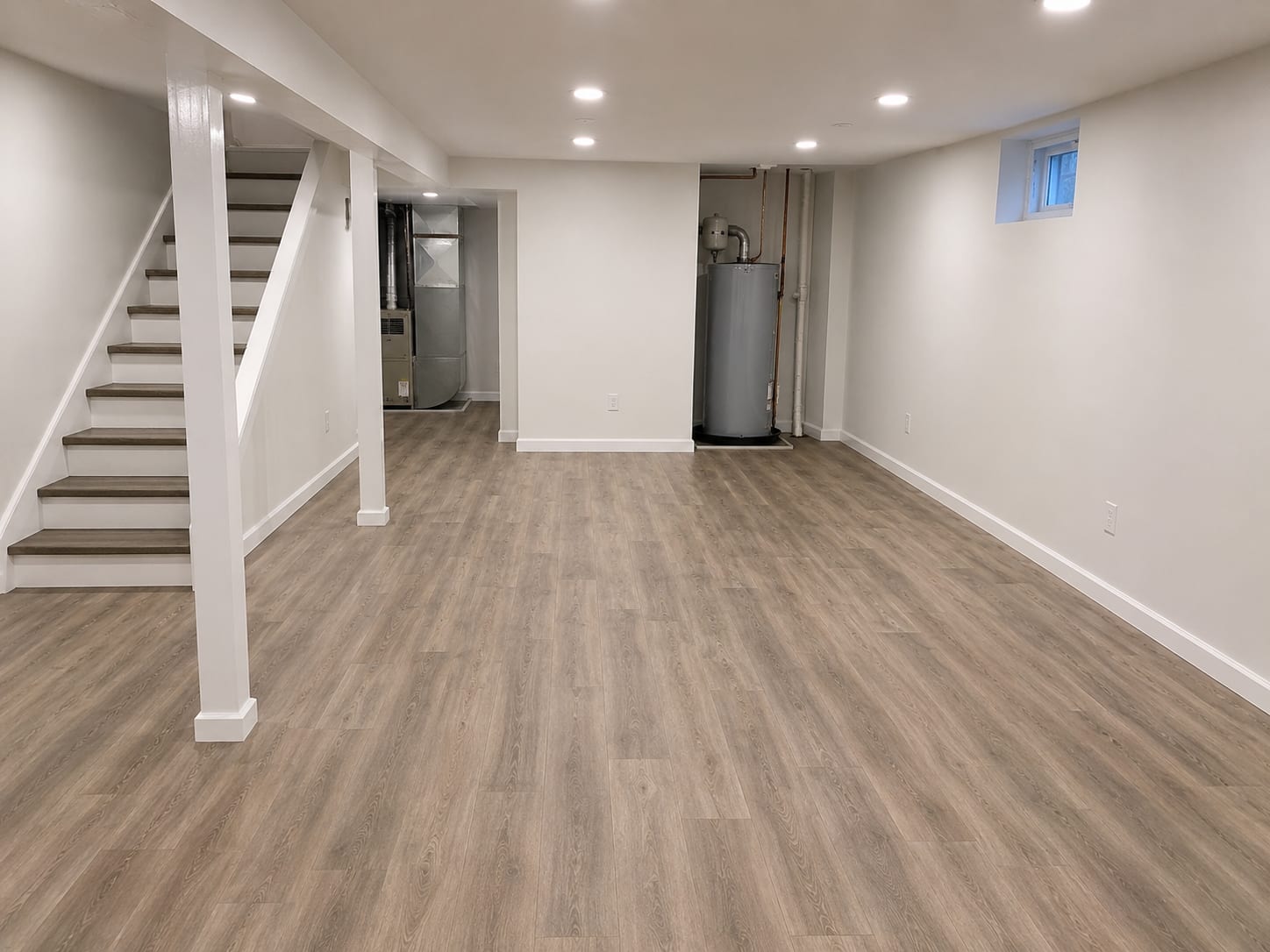 Freshly rebuilt and painted residential basement interior with new drywall, clean flooring, and bright overhead lighting after flood remediation
