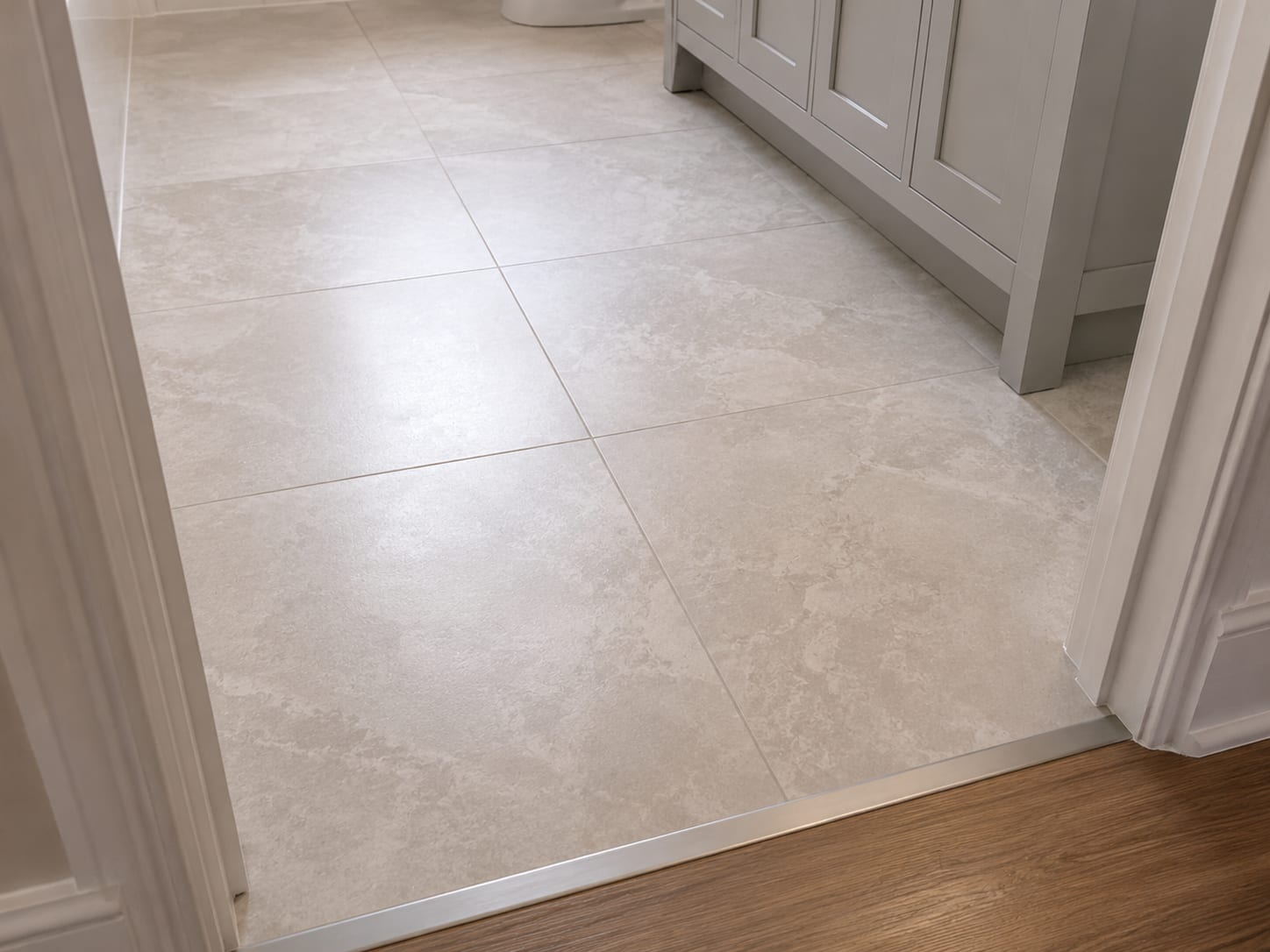 Freshly laid large-format porcelain floor tile with clean grout joints and a flush transition strip at the bathroom doorway threshold