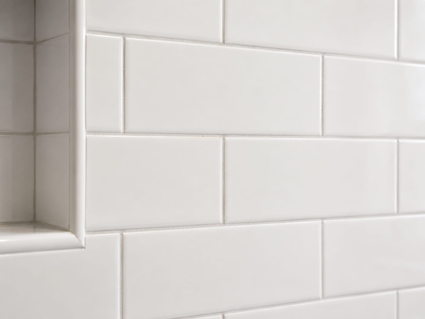 Close-up of freshly installed white ceramic wall tile with clean sanded grout joints and consistent spacing in a renovated bathroom